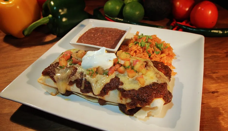 A burrito topped with sauce and melted cheese, with rice