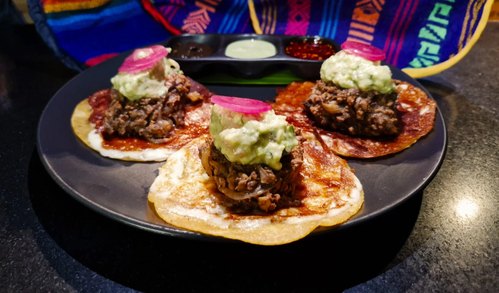 Three chalupas topped with beans, chorizo, guacamole and pickled onions