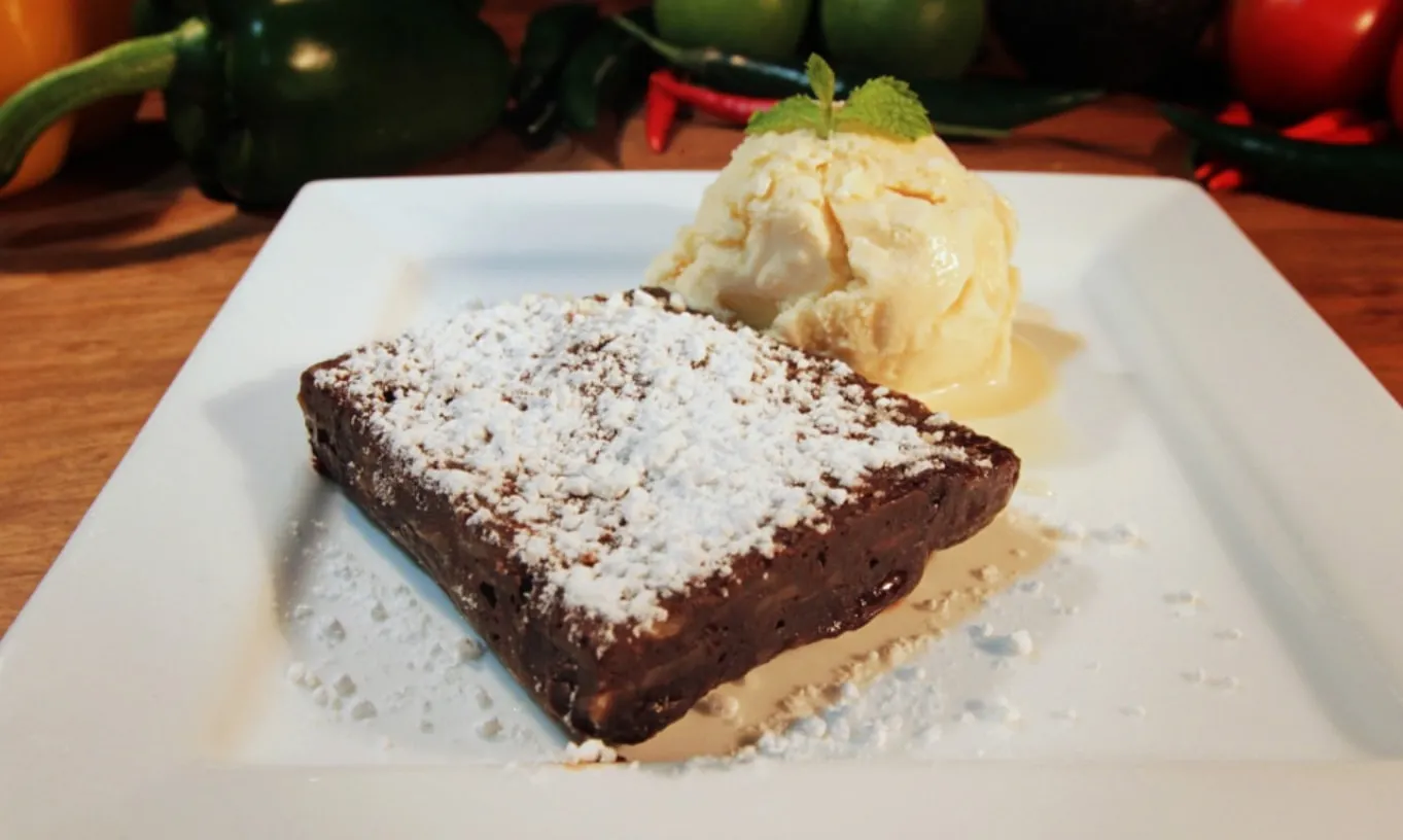 A dark chocolate brownie dusted with icing sugar, with a scoop of ice cream