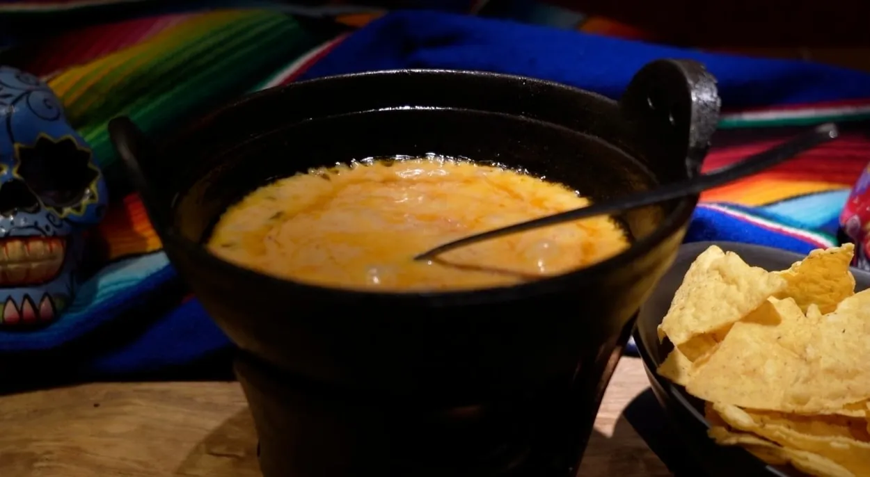 A pot of melted chili con queso with corn chips