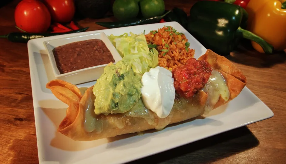 A chimichanga topped with guacamole, sour cream and salsa, with rice