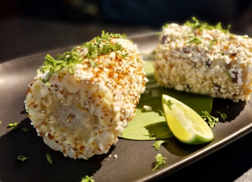 Two corn cobs coated in cheese and chilli with a wedge of lime