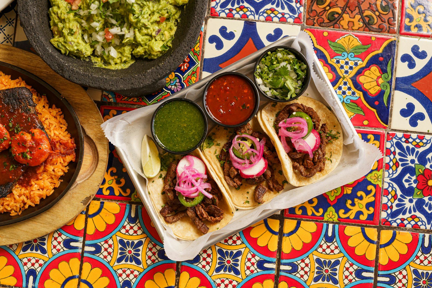 Tacos, salsas and guacamole on a colourful Talavera-tiled table