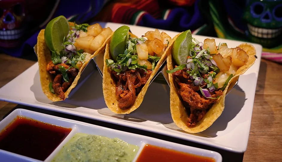 Three tacos al pastor with pineapple and three salsas